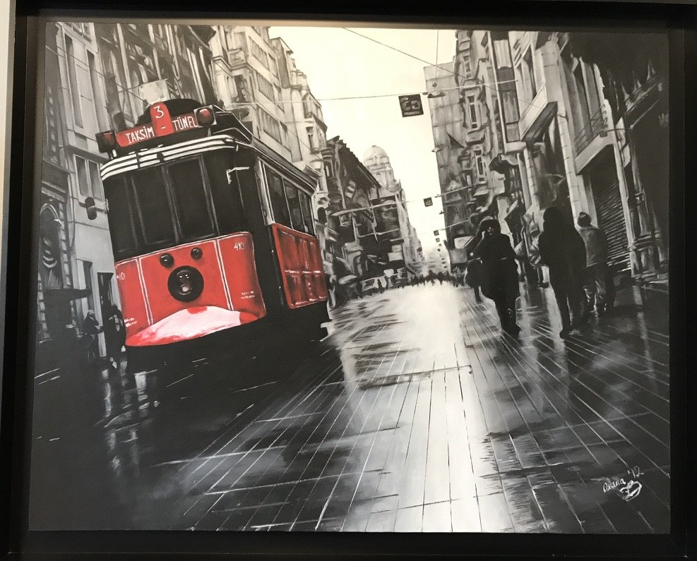 A red and black Istanbul tram on İstiklal Street, rendered mostly in black and white with the tram in color
