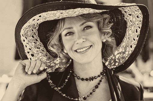 Portrait photograph of the painter Oxana Zaiats, wearing a wide-brimmed hat, toned in warm sepia