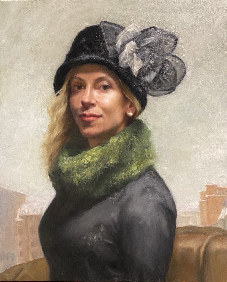 A woman in a black hat with a large bow, wrapped in a green scarf, against a city skyline