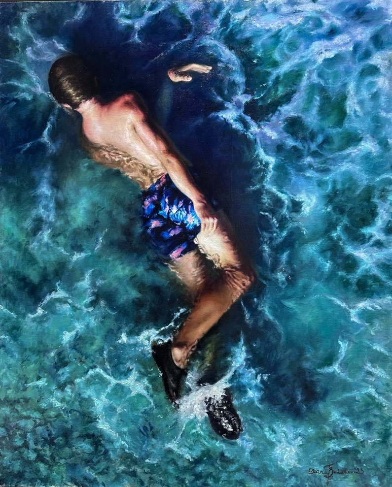A boy swimming underwater seen from above, in dark blue floral swim trunks amid turquoise waves